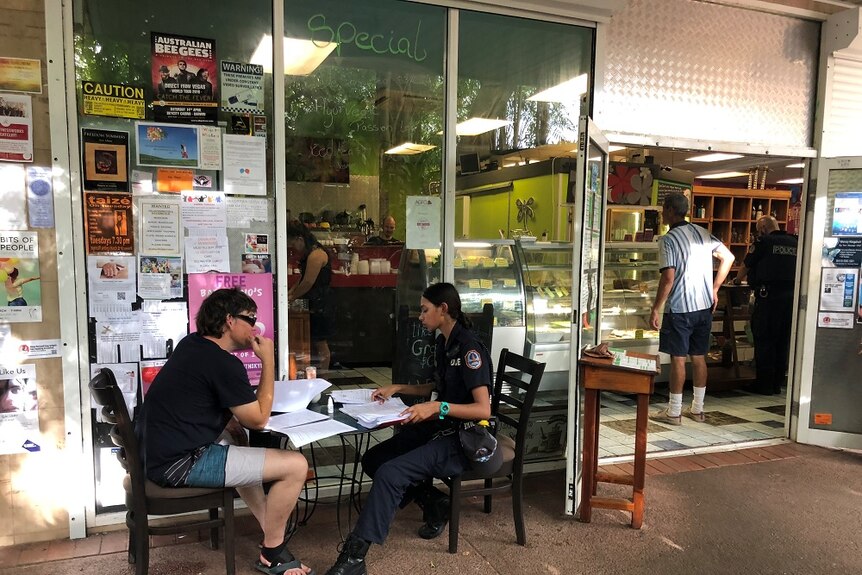 John Wharton sits with a police officer at a table out the front of the cafe as he gives a statement.