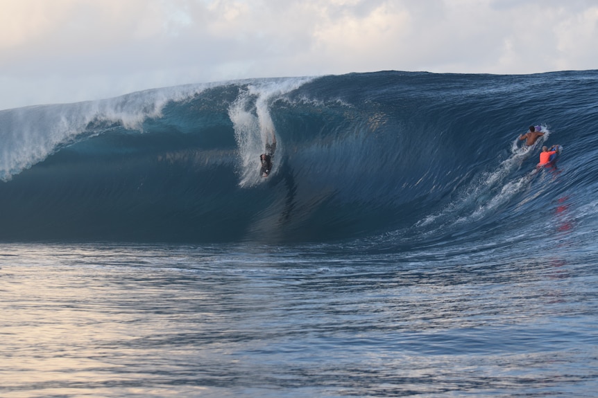 A man on a bodyboard dropping down the face of a huge wave.