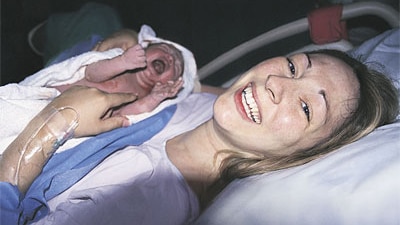 A woman, smiling, holding her newborn baby