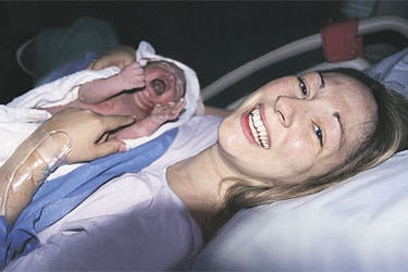 A woman, smiling, holding her newborn baby