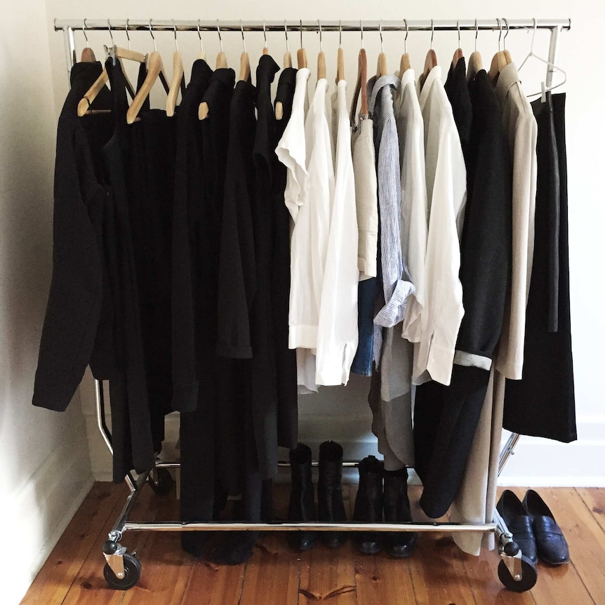 A clothes rack with black and white clothes and black shoes to depict a capsule wardrobe and personal uniform.