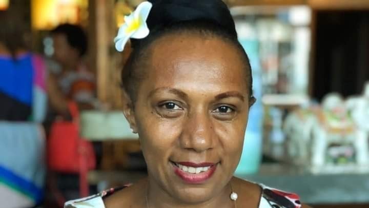 A woman wearing a floral white blue and pink dress with a frangipani behind her ear 