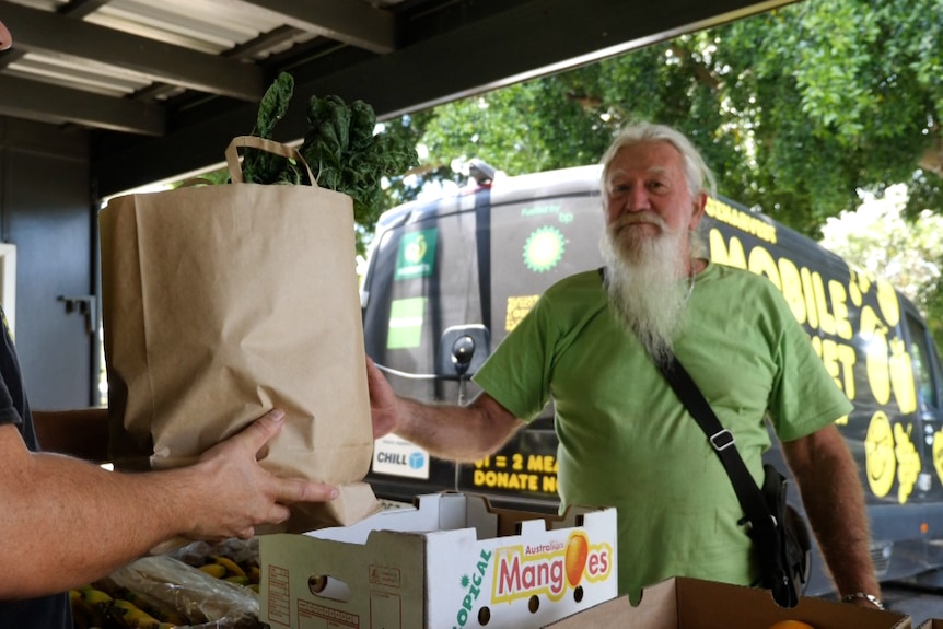 A man in a green shirt with a beard being handed a paper bag with kale