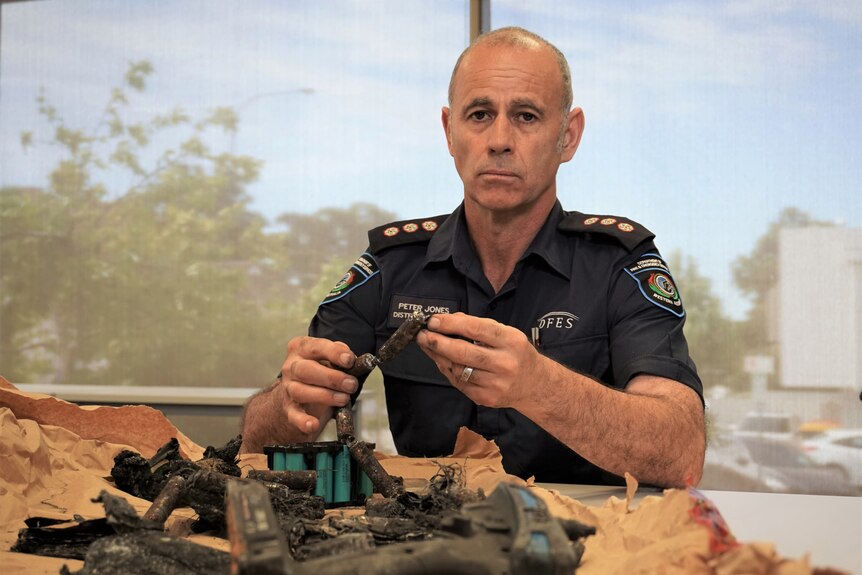 A man in a firefighter's uniform holding some charred batteries. 
