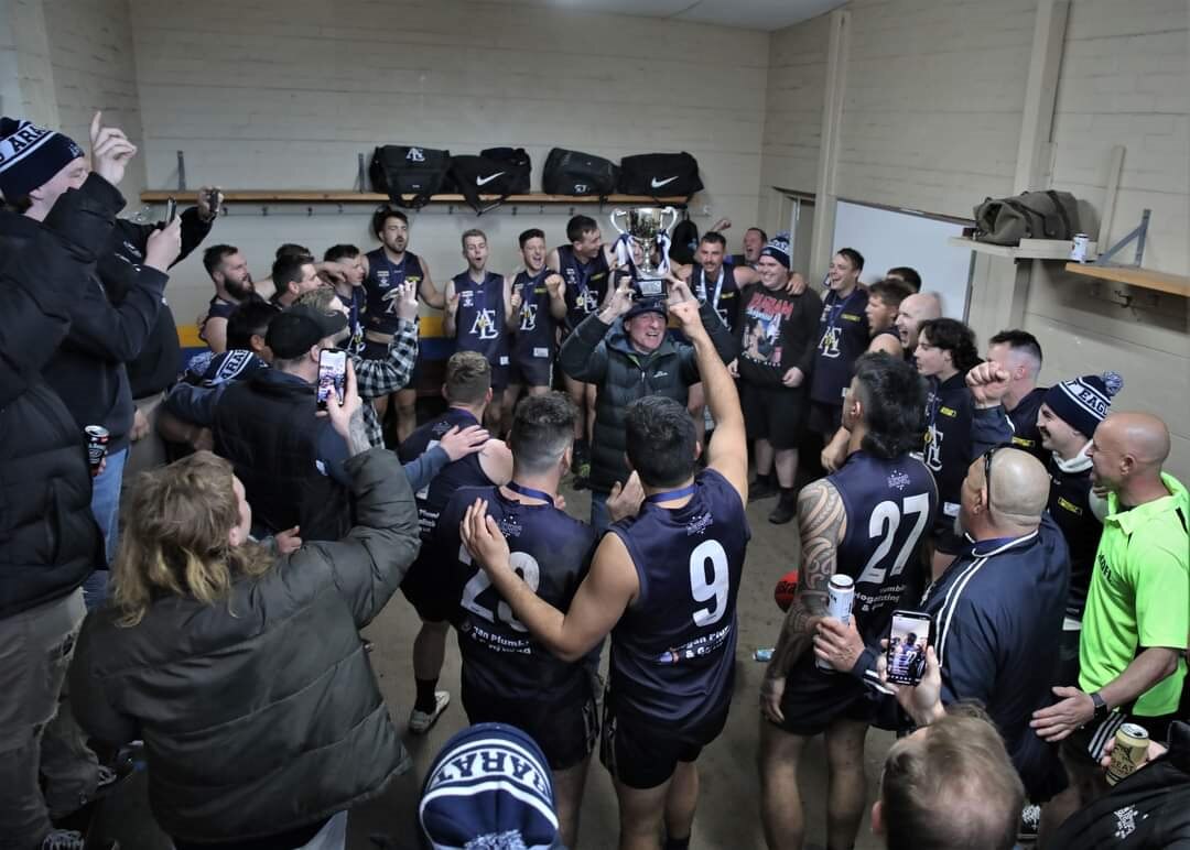 A football team wearing blue jersey in a club room huddle.