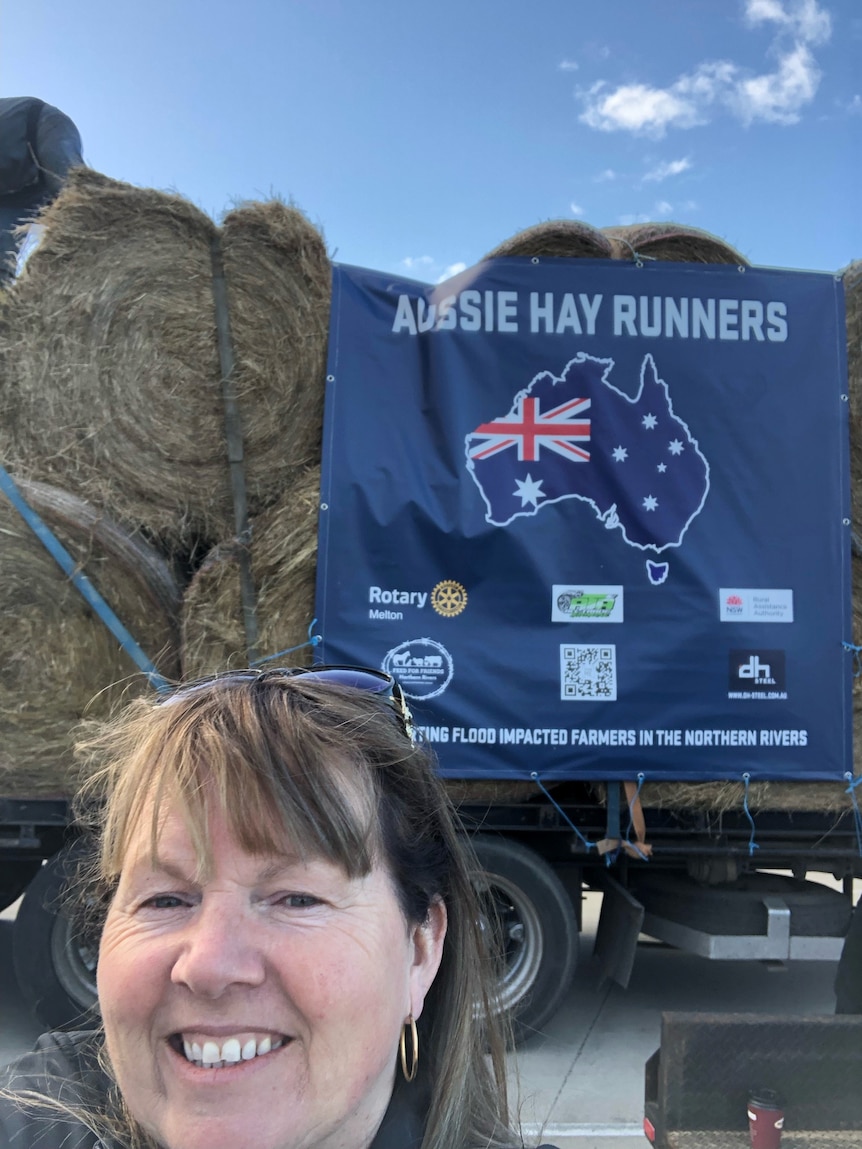 A selfie taken by a white woman with light brown hair and a straight fringe standing in front of a truckload of hay.