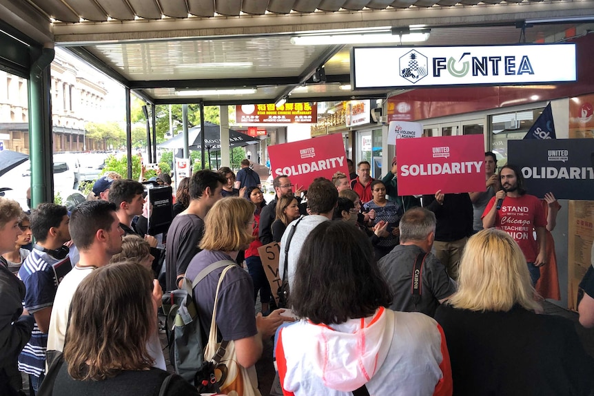 A crowd, assembled undercover in front of a Fun Tea store in Adelaide's CBD, holding signs saying 'solidarity'.