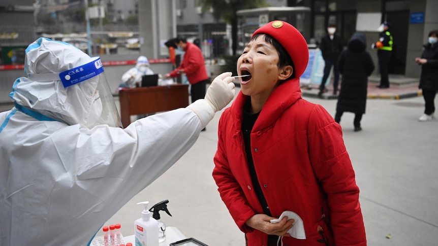 A woman in a red coat and hat gets a throat swab. 
