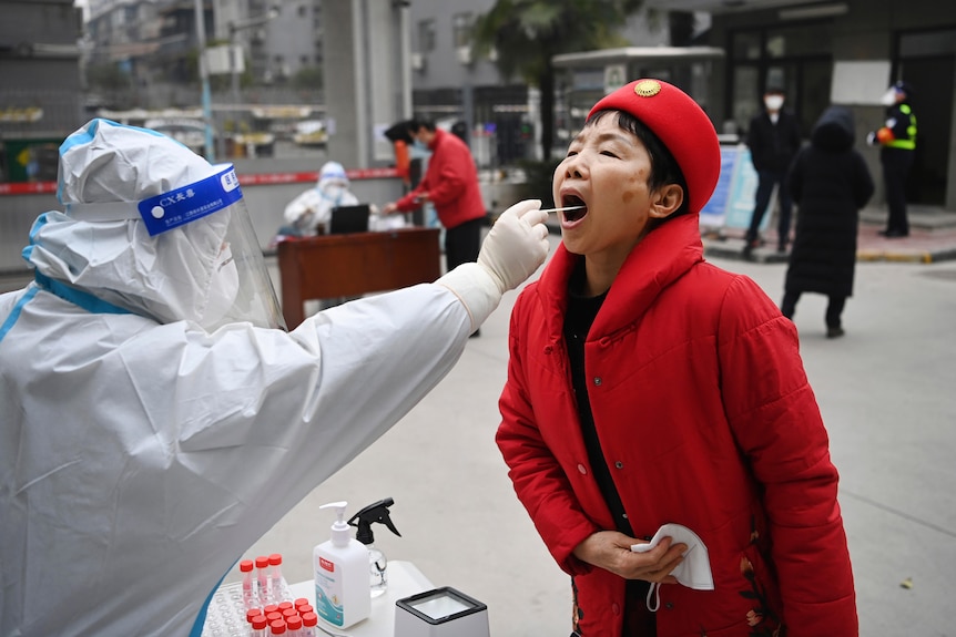 A woman in a red coat and hat receives a throat swab. 
