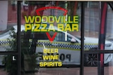 A police car reflected in the window of a pizza restaurant
