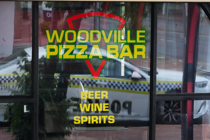A police car reflected in the window of a pizza restaurant