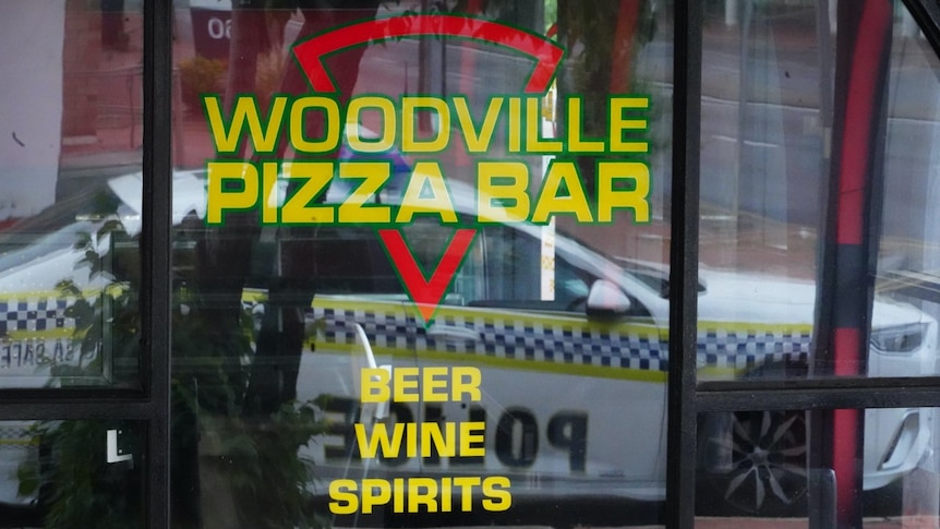 A police car reflected in the window of a pizza restaurant