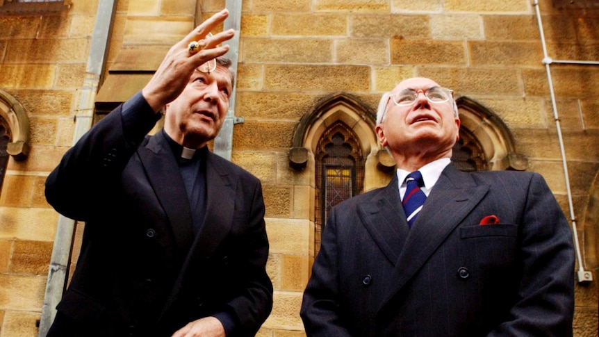 George Pell and John Howard pictured in front of a building, speaking to one another.