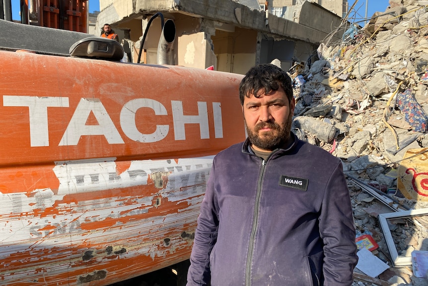 A man in a jumper stands next to an excavator 