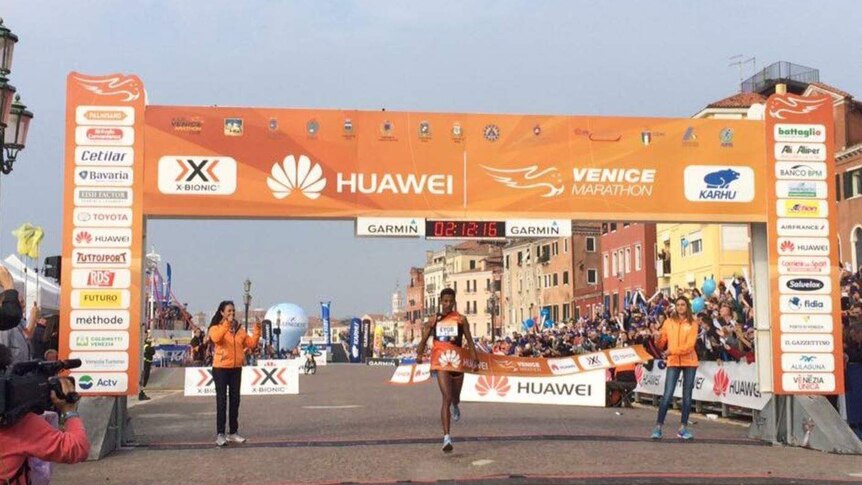 Crowds cheer as Eyob Faniel runs through an orange banner to mark the end of the Venice Marathon.