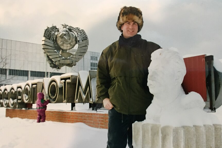 a man in winter clothing smiling next to a snow sculpture of Stalin