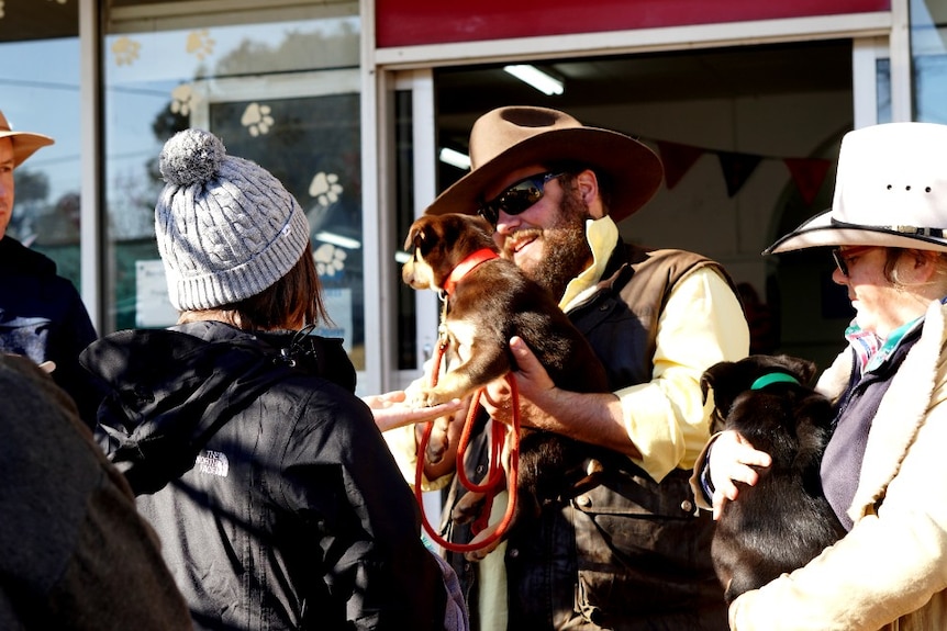 A man holding a puppy is surrounded by adoring fans on Casterton's main street during its 23rd Kelpie Muster