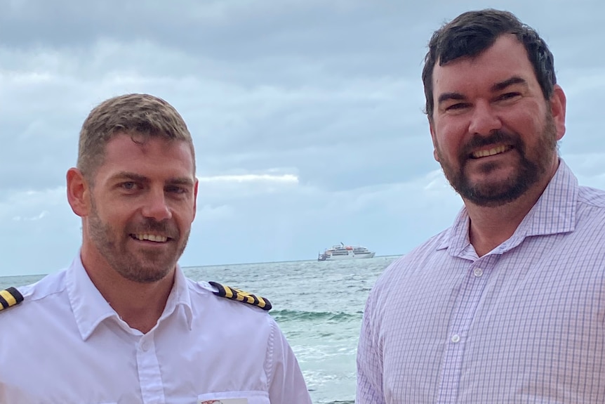 Two men standing in front of ocean with cruise boat in far distance