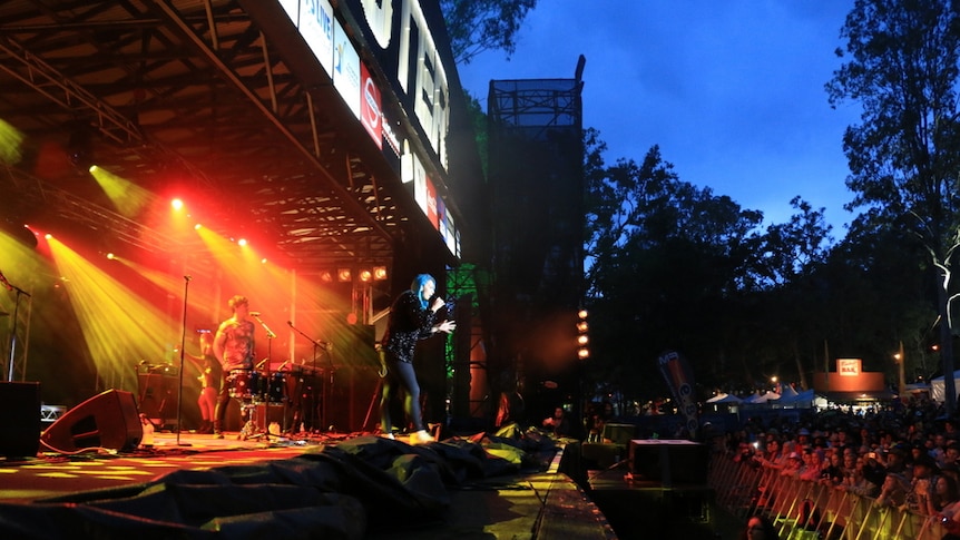 The band Sheppard are surrounded by yellow and orange lights on stage at the Gympie Muster in 2015.