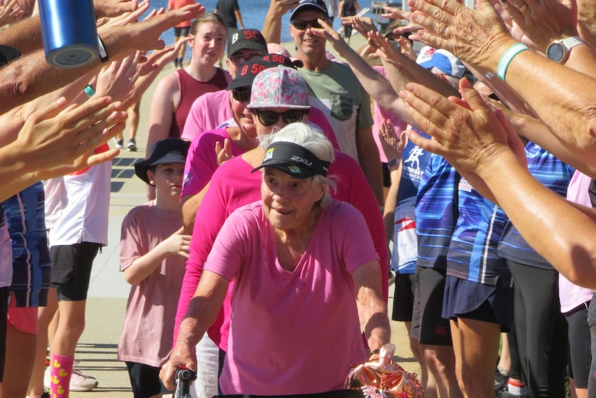 An elderly woman with a mobility walker finishes a walk with a guard of honour. 