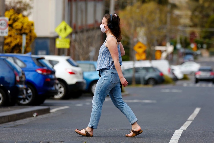 A woman wearing a face mask crosses a road in Melbourne.