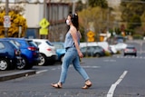 A woman wearing a face mask crosses a road in Melbourne.
