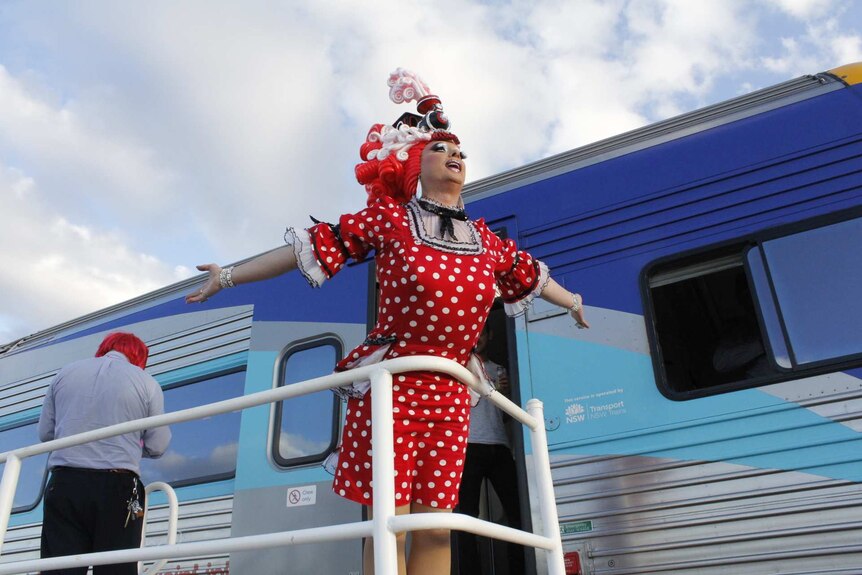 Drag queen poses next to the silver city stiletto train.
