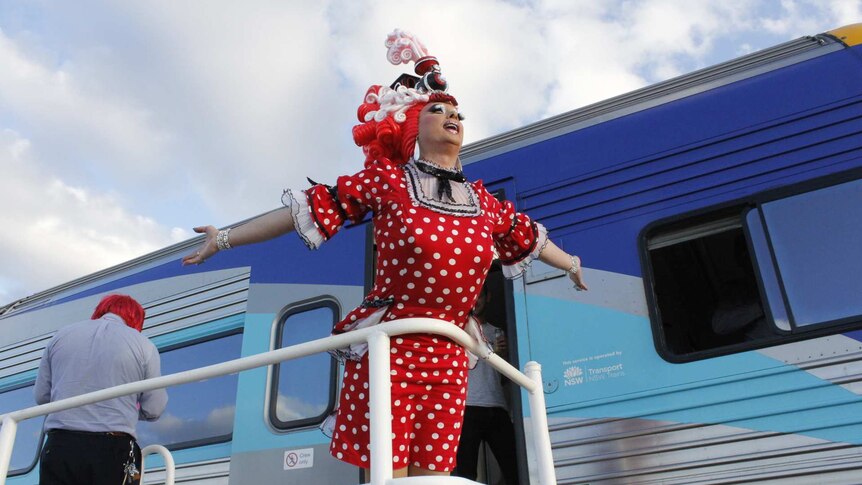 Drag queen poses next to the silver city stiletto train.