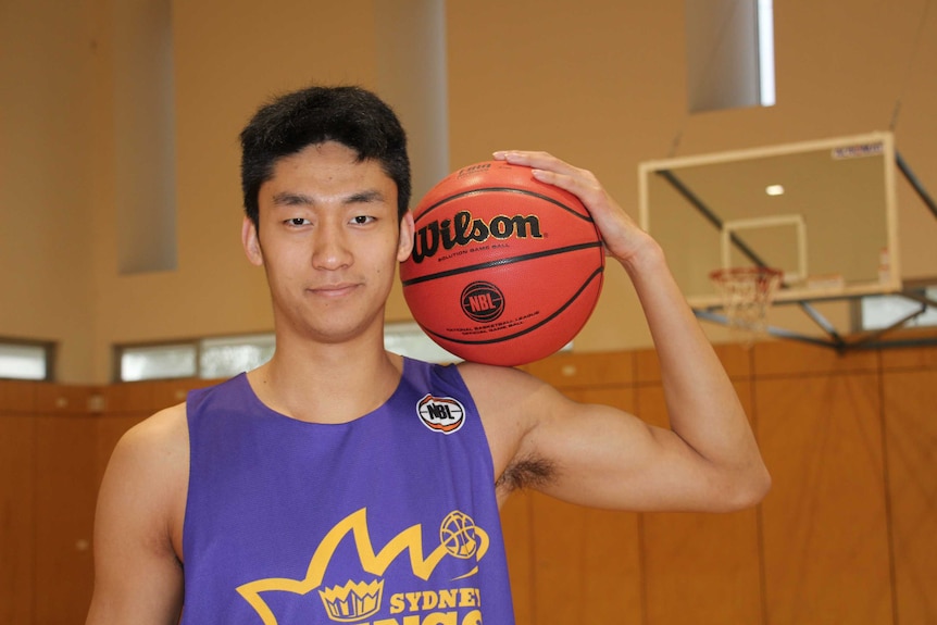 A Chinese man wearing a purple jersey holds a basketball