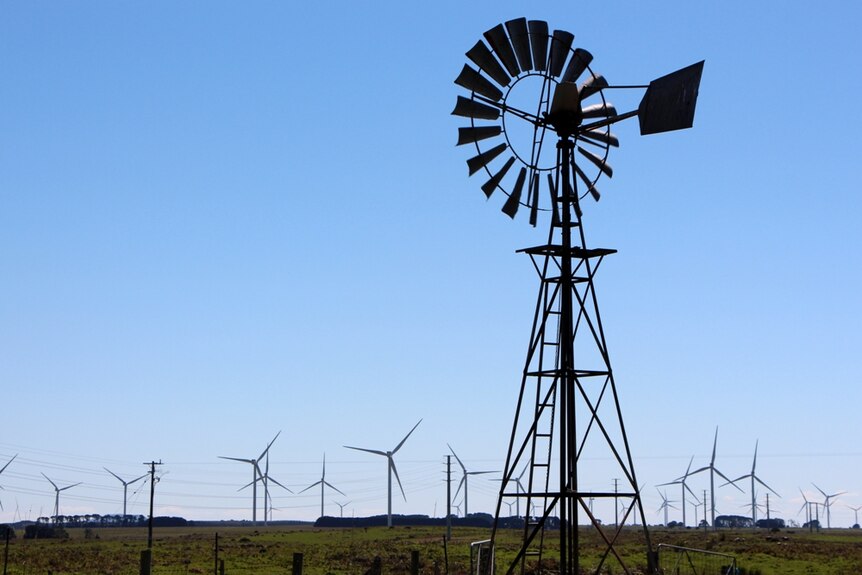 A windmill stands with wind turbines in the background