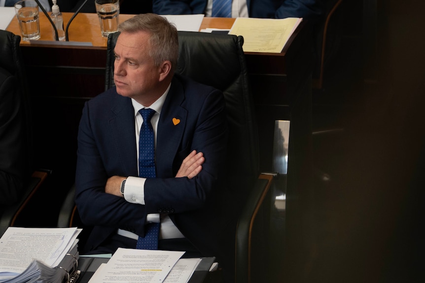 Jeremy Rockliff with arms folded looks off at someone else while sitting in parliament.