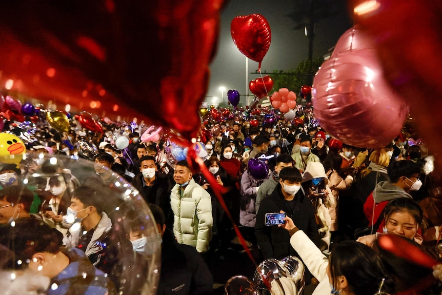 A crowd of hundreds hold balloons in the street to celebrate the new year.