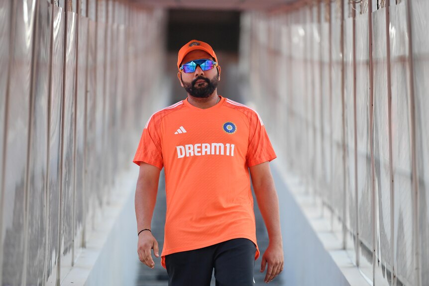 Indian cricket captain Rohit Sharma, wearing a cap and dark glasses, looks straight at the camera as he walks down steps.