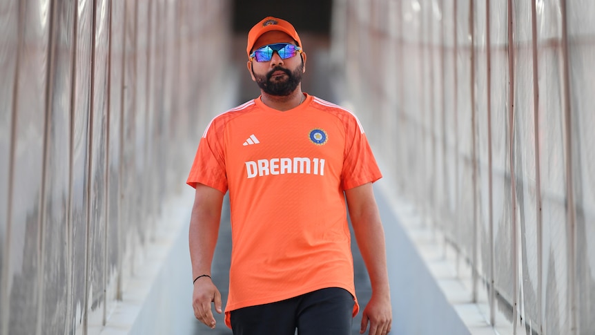 Indian cricket captain Rohit Sharma, wearing a cap and dark glasses, looks straight at the camera as he walks down steps.