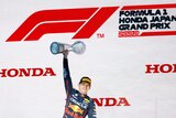 A Red Bull Formula One driver lifts a tropy in his right hand in front of Japan GP sign
