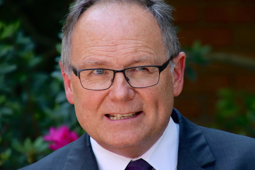 A close-up photograph of David Templeman dressed in a business suit and wearing glasses.