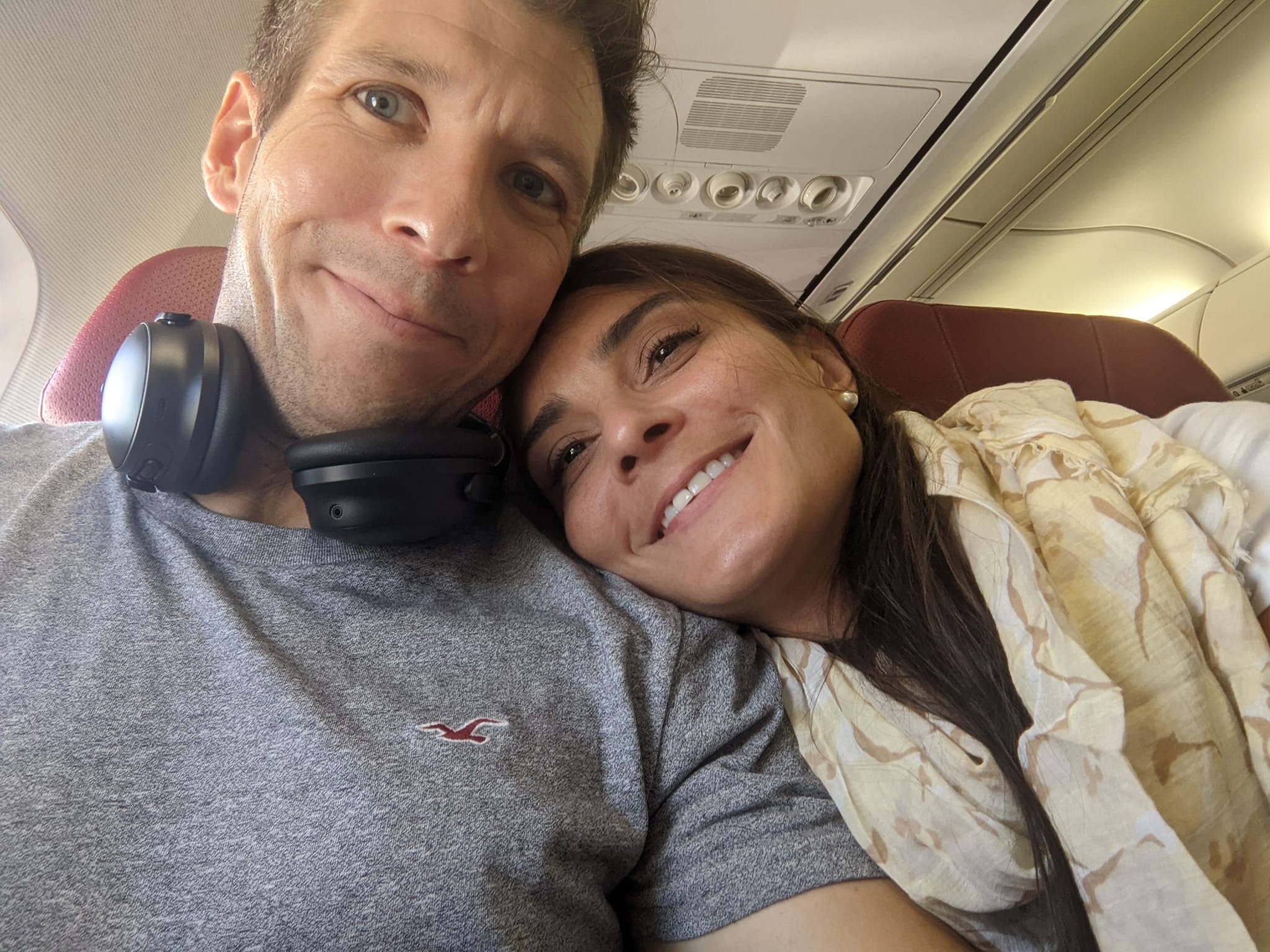 Un hombre y una mujer se toman un selfie en un avión, con la cabeza apoyada en su hombro.
