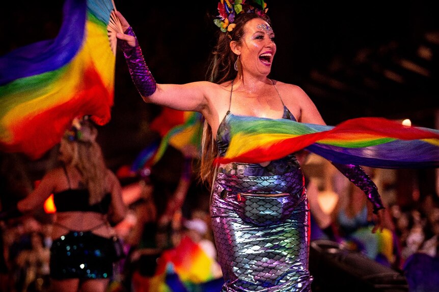 a woman carrying a rainbow flag wearing a glittery dress