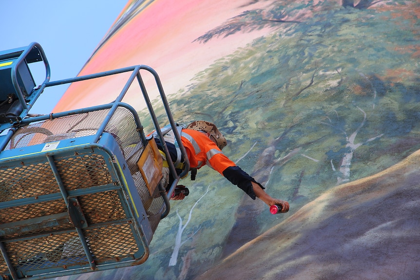 A man reaches out to spray paint a mural