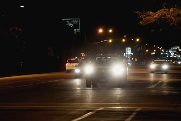 Cars driving on the left side of the road at night with their headlights on.