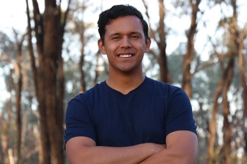 A man with wavy black hair and tanned skin, looks to the camera.