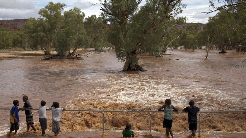 Children play on a causeway on the swollen Todd River