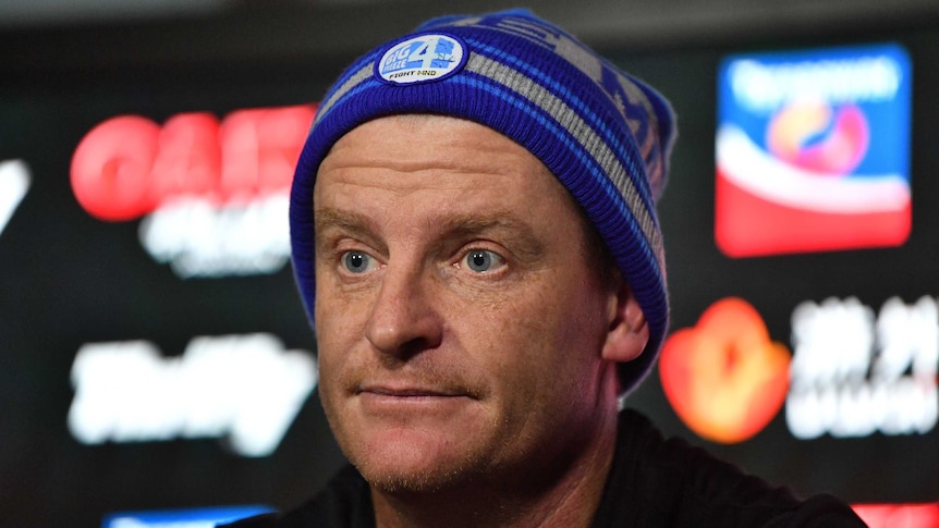 Man in a beanie sits at a table in a press conference.