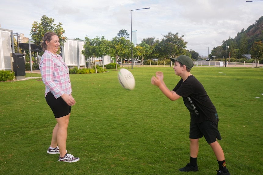 A woman and a young boy throw a rugby ball to each other in a park
