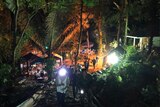 View at night of people walking up a rustic staircase on a hill in hte jungle, with lights and tents below