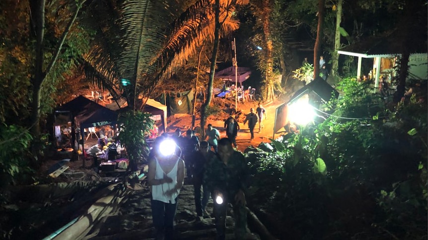 View at night of people walking up a rustic staircase on a hill in hte jungle, with lights and tents below