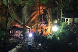 View at night of people walking up a rustic staircase on a hill in hte jungle, with lights and tents below