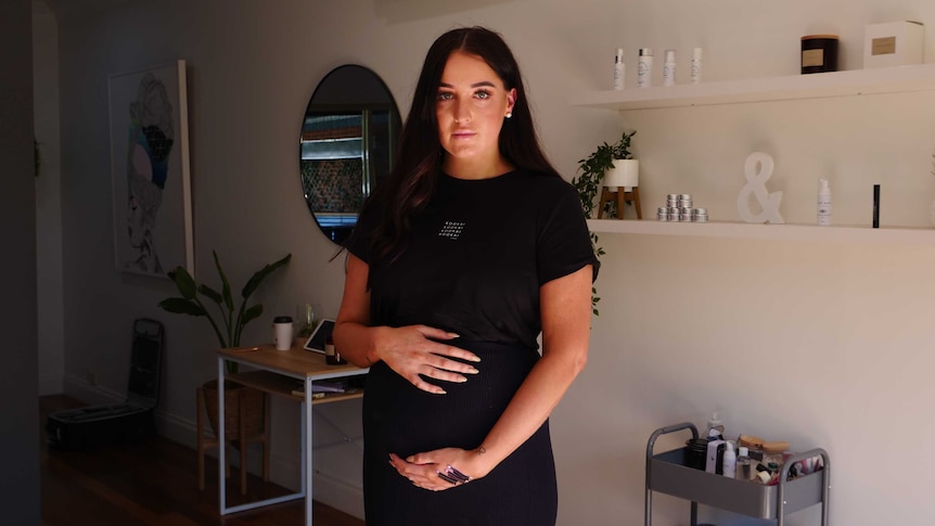 Lucy Pallot standing in her beauty salon cradling her pregnant stomach