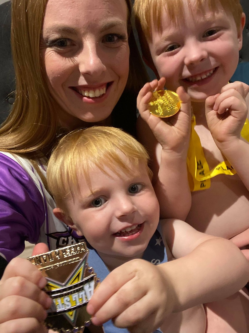 Selfie of mum with two toddlers holding medals and smiling. 