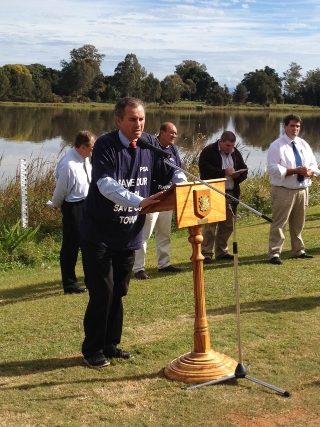 A man, surrounded by other men, speaking into a microphone in the Clarence Valley